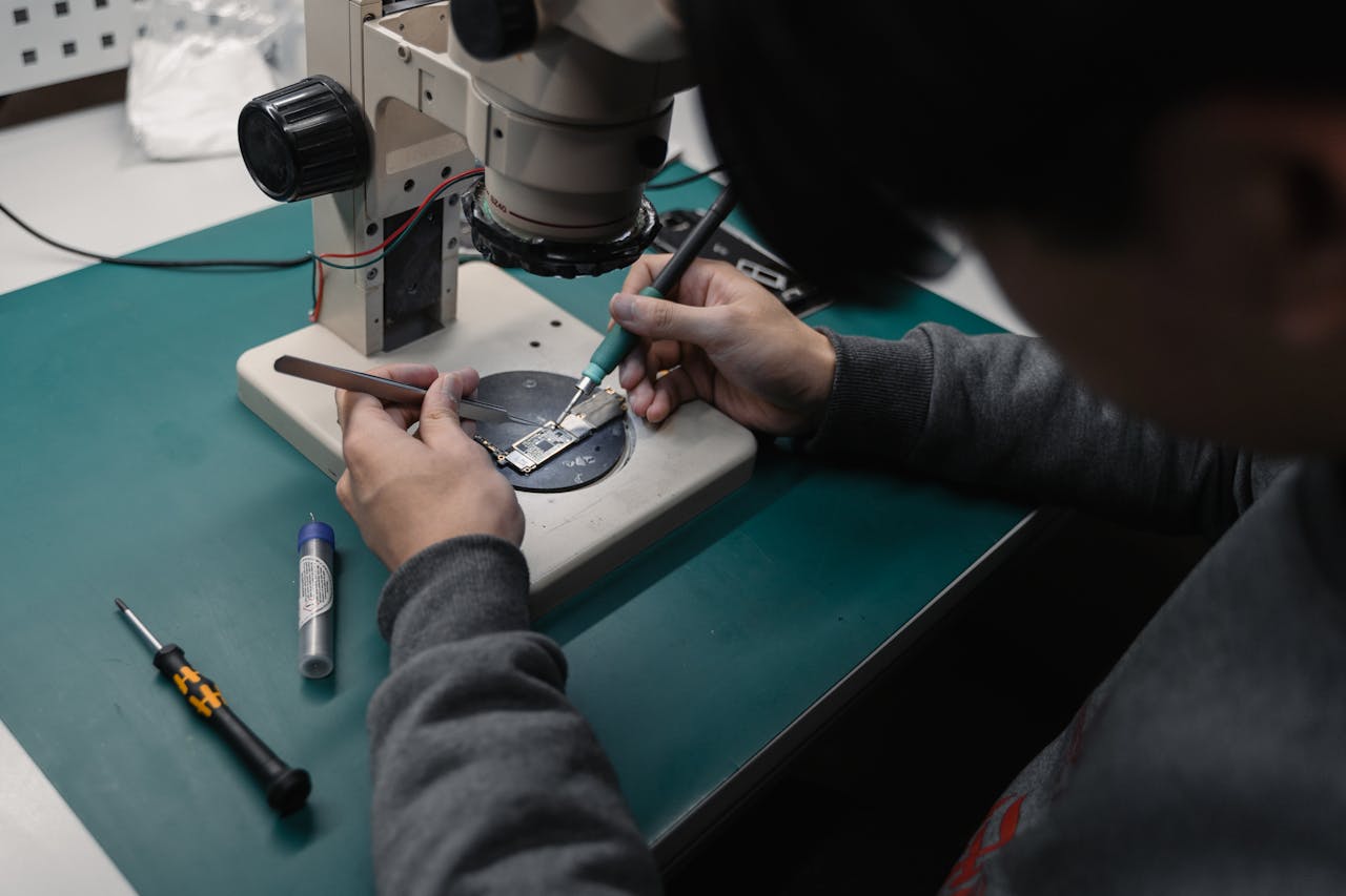 about-img Technician using a microscope to repair a broken electronic board with precision tools.